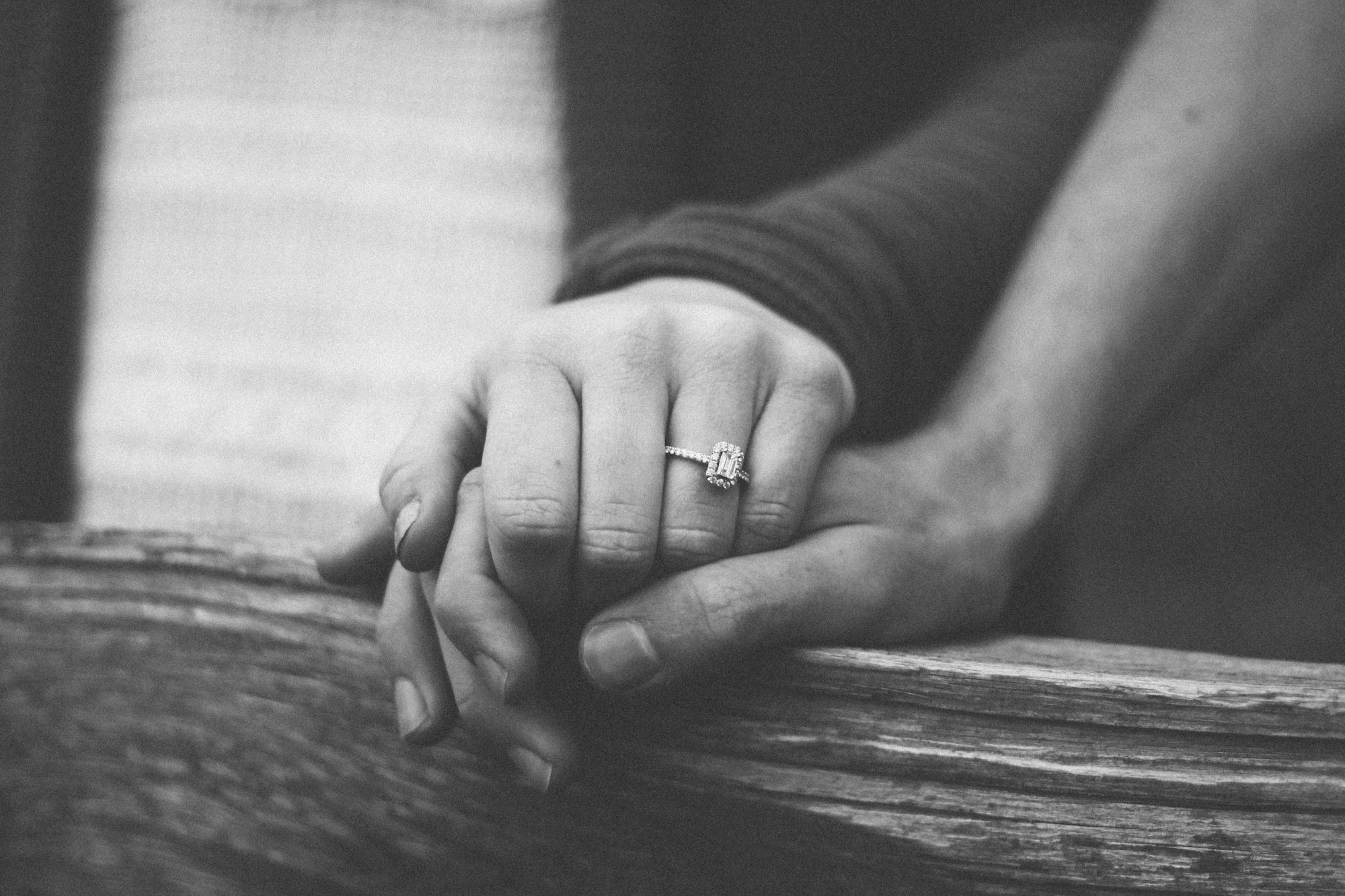 Two hands resting together, an engagement ring in soft focus